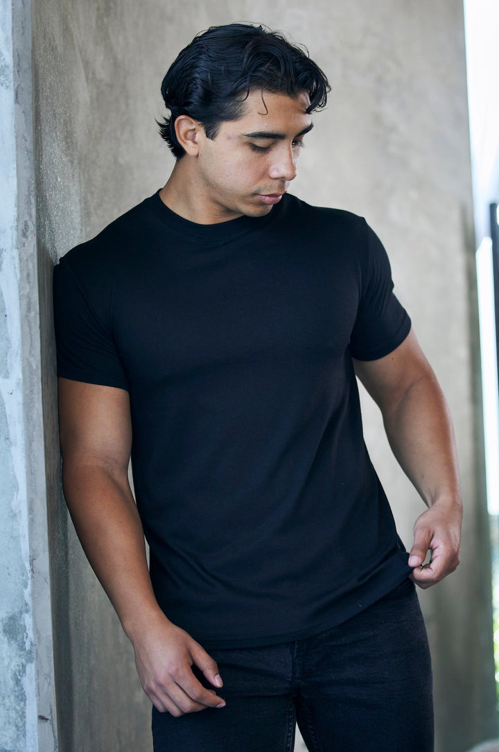 Man wearing a black bamboo t-shirt  standing against a wall 